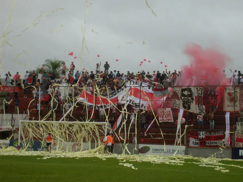 La hinchada detrás de un arco entre serpentinas, banderas y humo de bengalas.